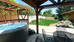 Une terrasse couverte avec un jacuzzi, du mobilier d’extérieur et une vue sur le jardin.