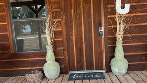 A wooden cabin with a dark brown door, a window, and a welcome mat. - Cope's Haven (Fredericksburg)