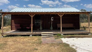 A rustic cabin with a metal roof, wooden deck, and a porch with a bench. - Cope's Haven (Fredericksburg)