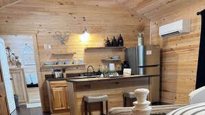 A cozy cabin interior with a wooden interior, a kitchen area with a refrigerator, and a bed with striped bedding. - Cope's Haven (Fredericksburg)