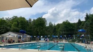 A swimming pool with multiple lanes, surrounded by trees and a covered area with umbrellas. - Casa Vines (DrPocono Lake)