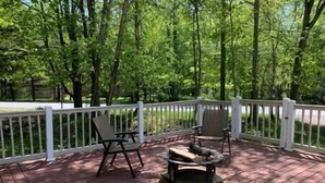 A wooden deck with two chairs and a fire pit, surrounded by a white railing and lush greenery. - Casa Vines (DrPocono Lake)