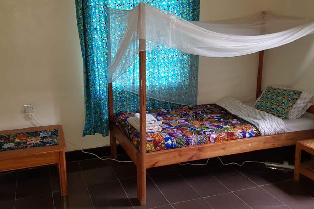 Ein hölzernes Himmelbett mit farbenfroher Steppdecke, ein Nachttisch, eine Lampe und Vorhänge.