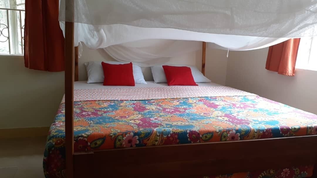 A bed with a canopy, red and white pillows, and a colorful floral bedspread.