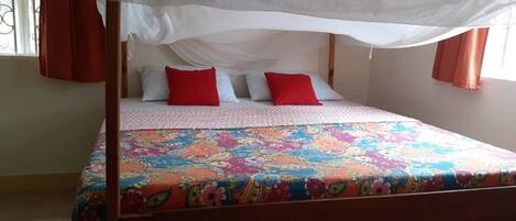 A bed with a canopy, red and white pillows, and a colorful floral bedspread.