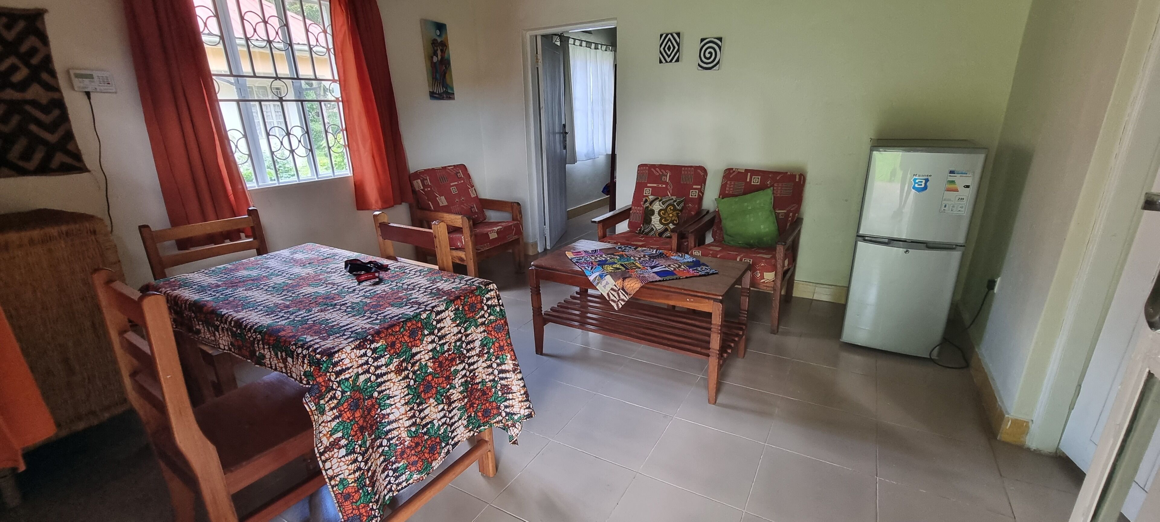 Un comedor con una mesa cubierta por un mantel estampado, sillas de madera y un refrigerador.