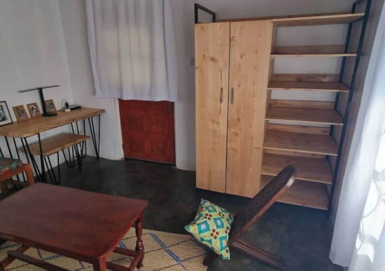 A room with a wooden staircase, a dining table with chairs, a red cabinet, and a patterned rug.