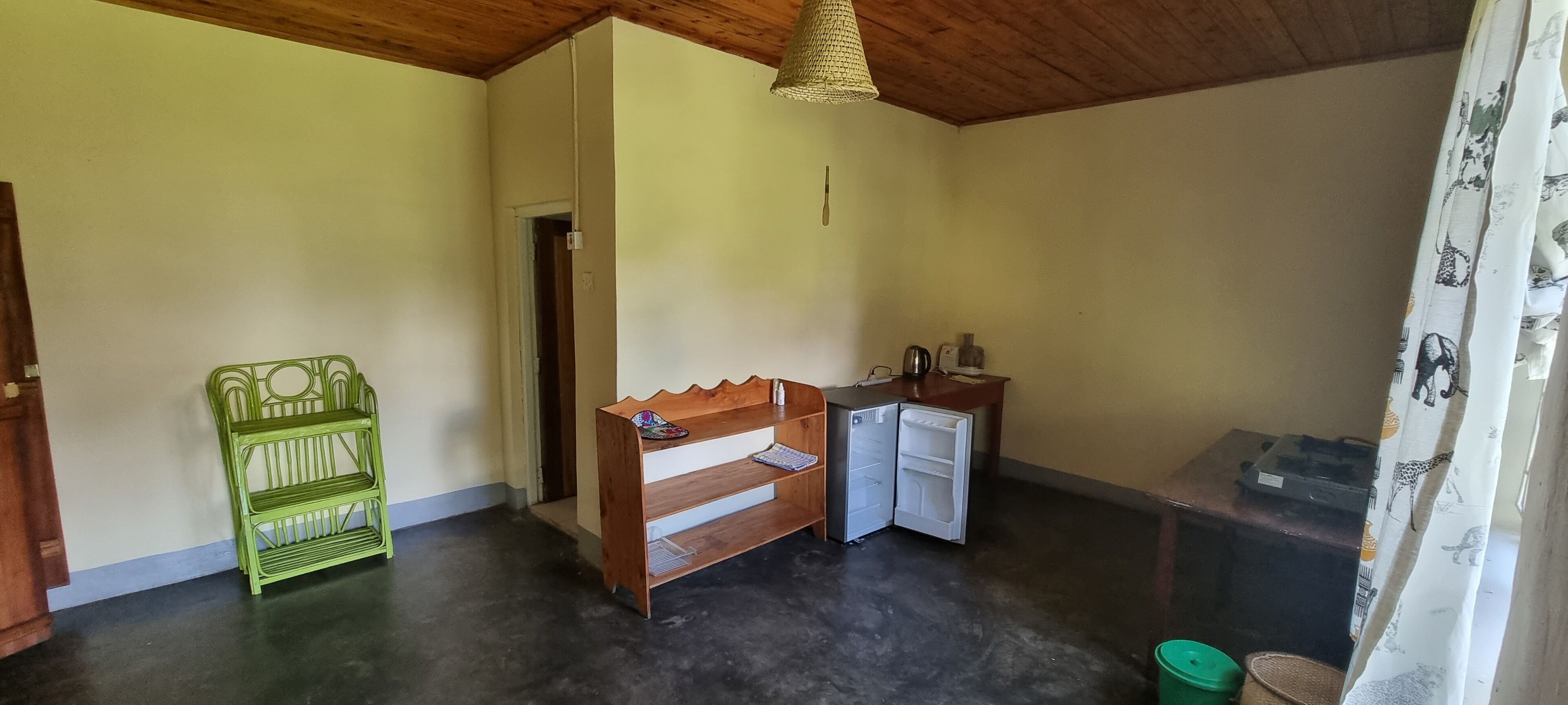 Una habitación pequeña y funcional con un banco de madera, un refrigerador pequeño y una silla verde.