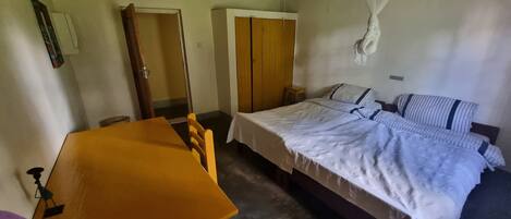 A bedroom with a bed, a wooden table, a chair, a wardrobe, and a hanging mosquito net.