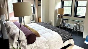 Una habitación de hotel con cama, escritorio, silla, ventilador de techo y ventanas grandes.