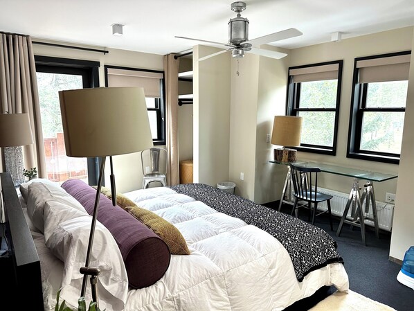 Ein Hotelzimmer mit Bett, Schreibtisch, Stuhl, Deckenventilator und großen Fenstern.