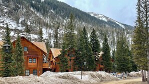 Un lodge rústico con varias cabañas de madera, rodeado de montañas nevadas y densos bosques de pino.