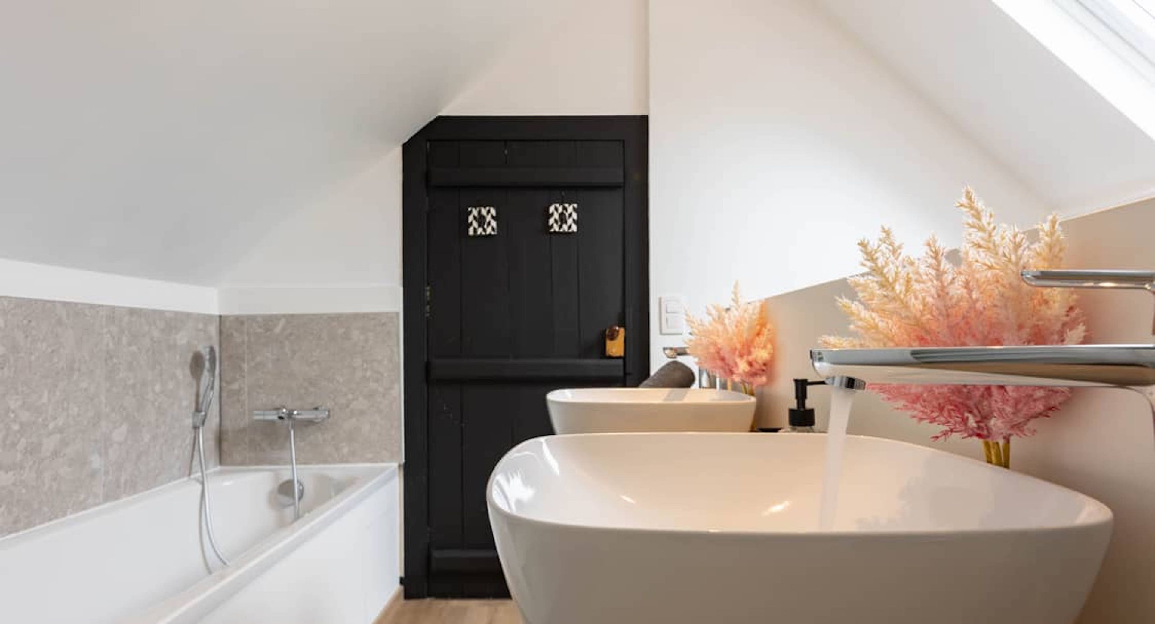 A modern bathroom with a freestanding bathtub, a large white sink, and a black door with decorative patterns.