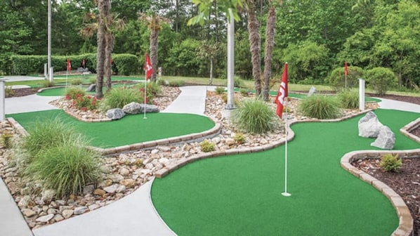 A miniature golf course with green artificial turf, red flags, and landscaped areas with rocks and plants. - Greensprings Resort (Williamsburg)