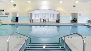 Una piscina interior con agua cristalina, un letrero que indica que no se permite bucear, y una zona junto a la piscina con sillas y una mesa.