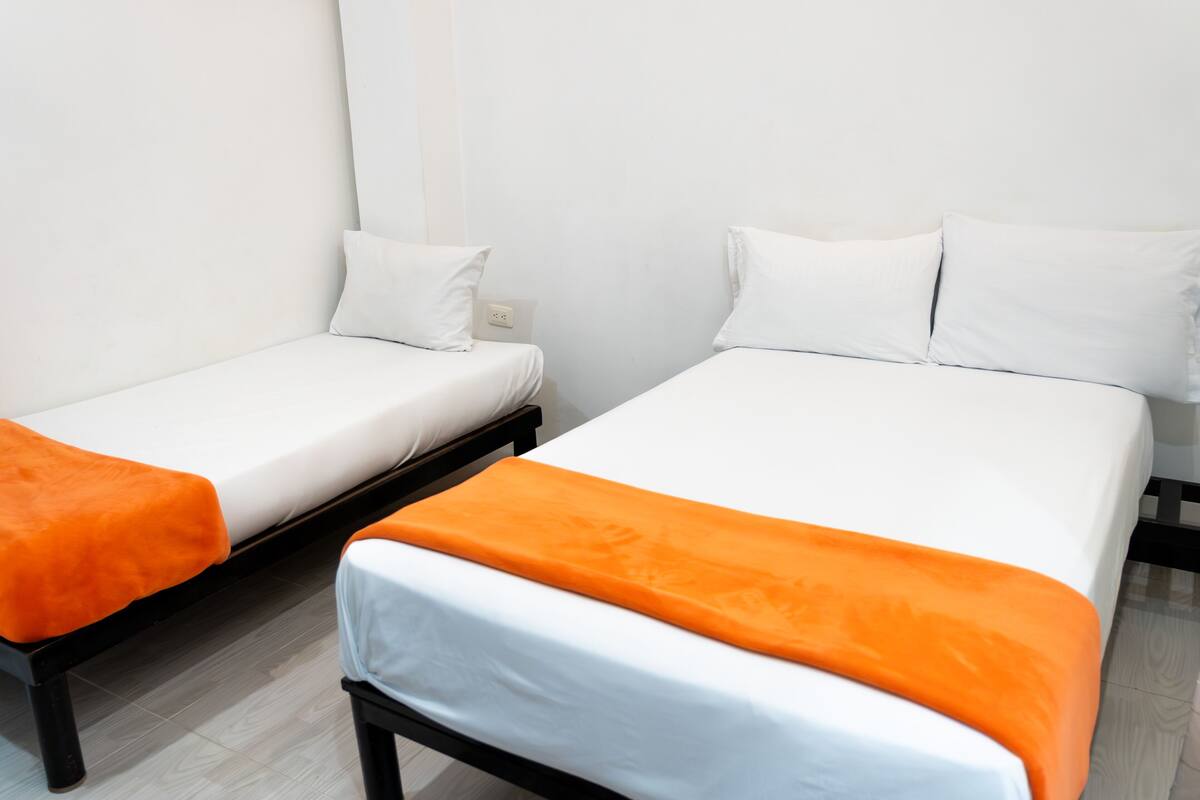 Deux lits simples avec une literie blanche et des coussins décoratifs orange, un banc noir et un mur blanc.