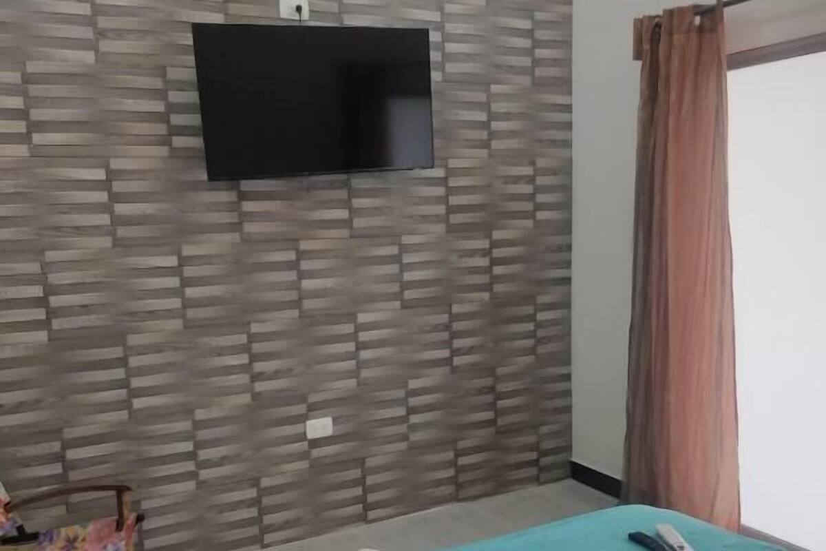 Une chambre d’hôtel comprenant un lit, un téléviseur à écran plat fixé au mur, une fenêtre avec des rideaux et une petite table avec une chaise.
