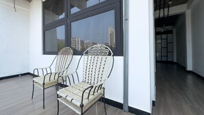 Two wicker chairs with metal frames and woven seats, positioned in front of a large window with a view of buildings and a clear sky.
