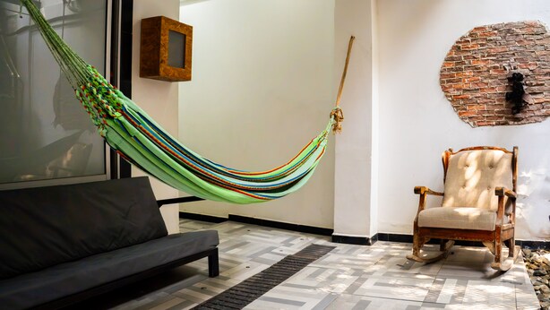 A room with a hammock, a wooden rocking chair, a sofa, and a patterned floor.