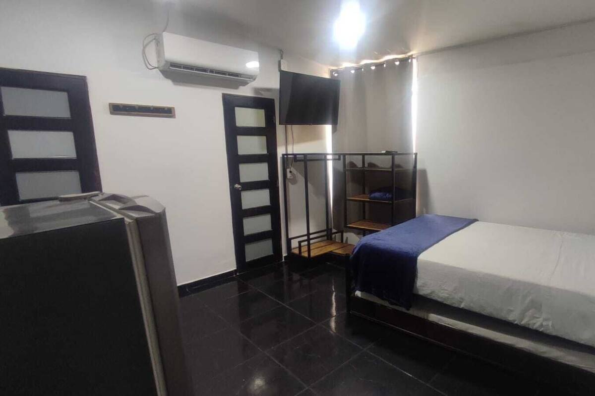 Une chambre d’hôtel de taille réduite, comprenant un lit, une armoire, un bureau et une petite kitchenette.