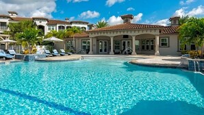 Una piscina con sillas de descanso y sombrillas, rodeada de edificios de estilo mediterráneo.