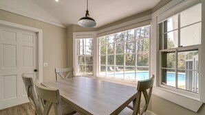 A dining area with a wooden table and chairs, large windows with a view of a swimming pool and trees, and a white door. - Wilmington Rental ~ 4 Mi to Wrightsville Beach! (Wilmington)