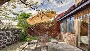 En terrasse med et bord og stole, en stor parasol og en mur af trælameller.