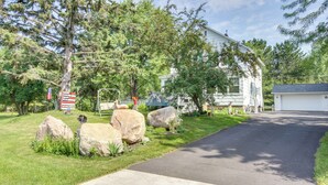 En indkørsel fører til et hus med garage, omgivet af store sten og træer.