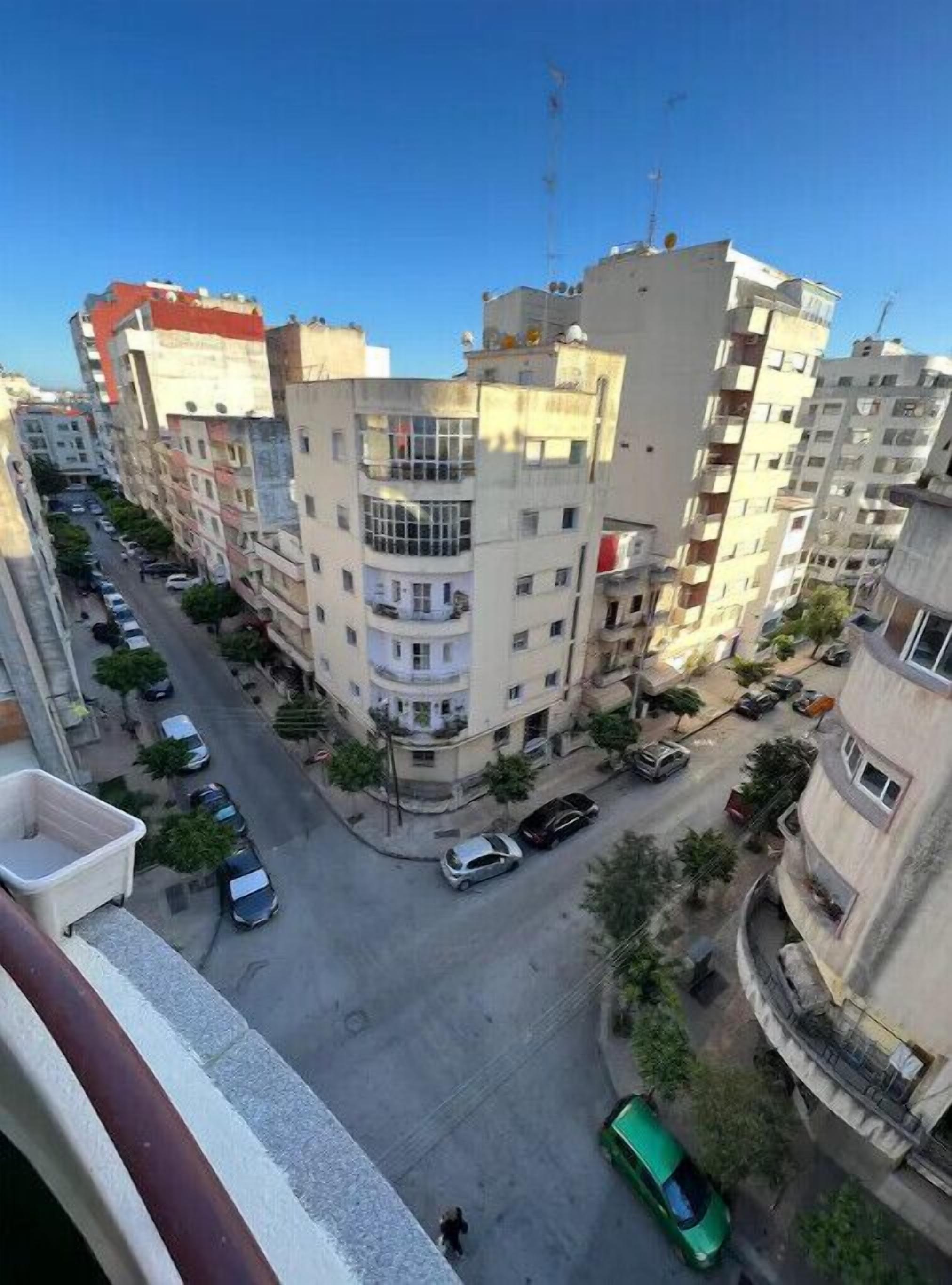 A multi-story residential building with balconies, a central courtyard, and a street with parked cars.
