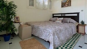 Ein Schlafzimmer mit einem Bett, einer Zimmerpflanze, einem Teppich und einer karierten Matte auf dem Boden.