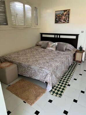 Una camera da letto con un letto, un tappeto, un pavimento a scacchi, un quadro appeso al muro e una finestra con persiane.