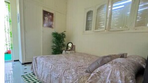 Ein Schlafzimmer mit einem Bett, einem karierten Teppich, einem kleinen runden Tisch mit einer Pflanze und einer Pendelleuchte.