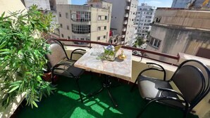 Ein Balkon mit Tisch und Stühlen, einem Blumentopf und Blick auf umliegende Gebäude.