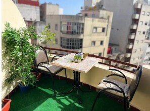 Un balcone con tavolo e sedie, un vaso con una pianta e vista sugli edifici circostanti.