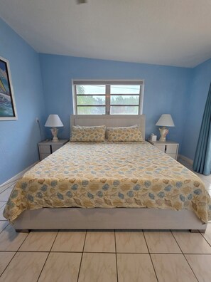 Une chambre à coucher avec un lit, deux tables de chevet, une fenêtre et un tableau au mur.