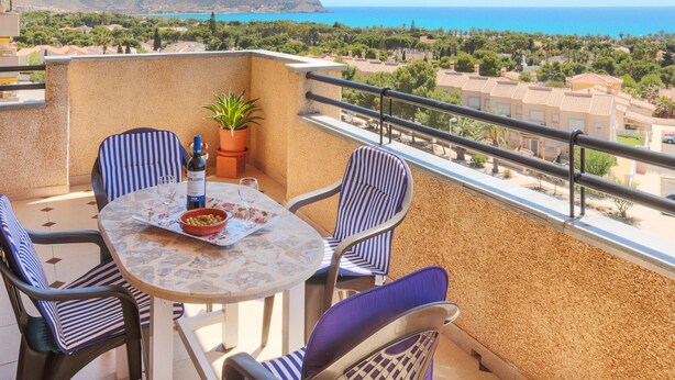 Un balcon avec une table, des chaises, une bouteille de vin et un bol d’olives.