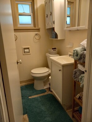 A small bathroom with a toilet, sink, and shelves with towels.