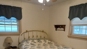 Une chambre à coucher avec un lit, une table de chevet, une lampe et un ventilateur de plafond.