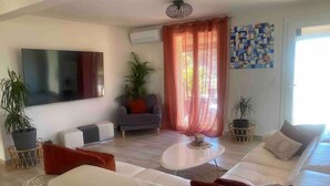 Una sala de estar moderna con un sofá blanco, un sillón gris, una mesa de centro y un televisor de pantalla plana grande montado en la pared.