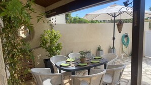 Un patio al aire libre con una mesa redonda para cuatro personas, rodeado de sillas de mimbre.