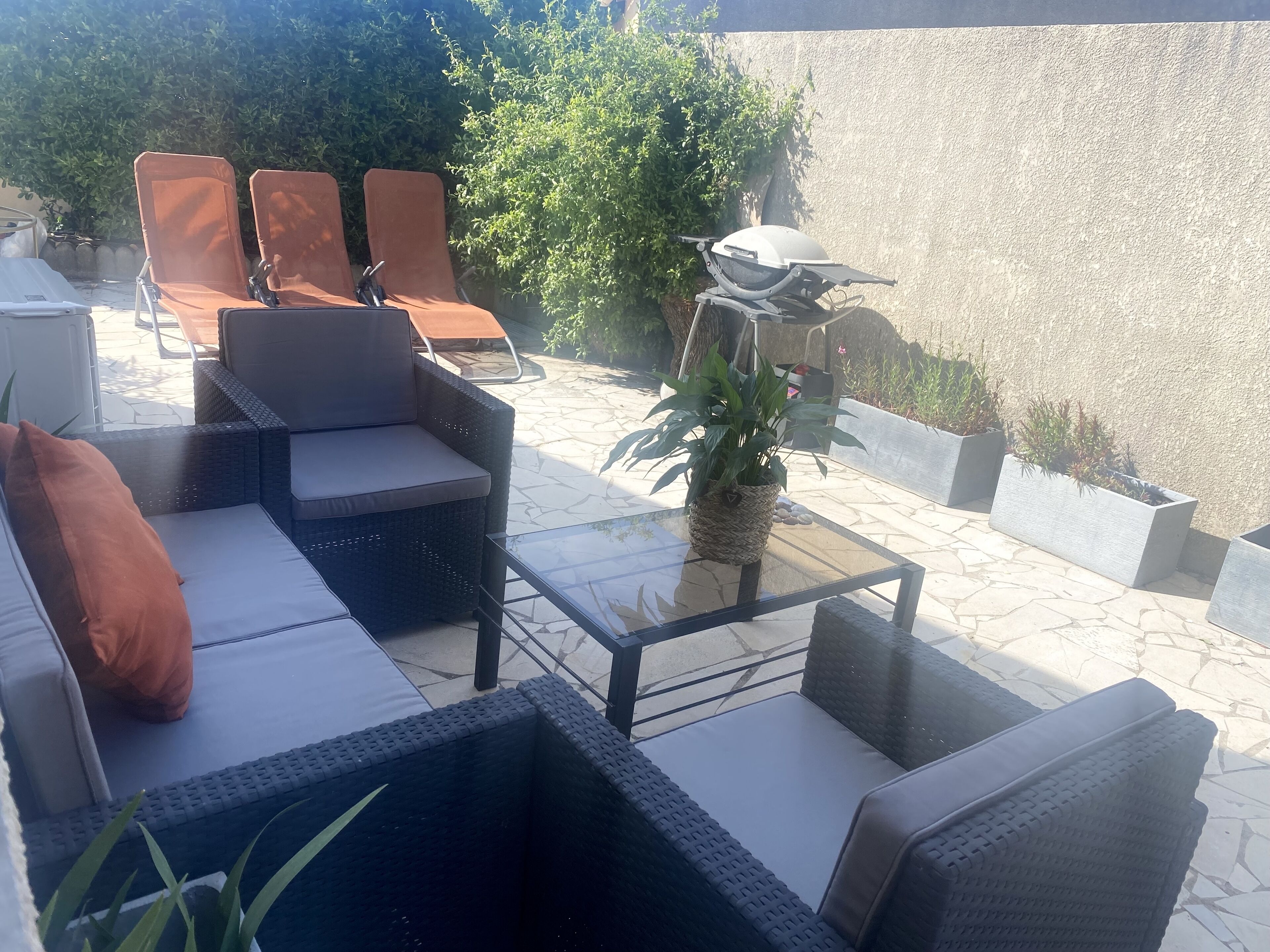 A patio area with wicker furniture, a glass table, and potted plants.