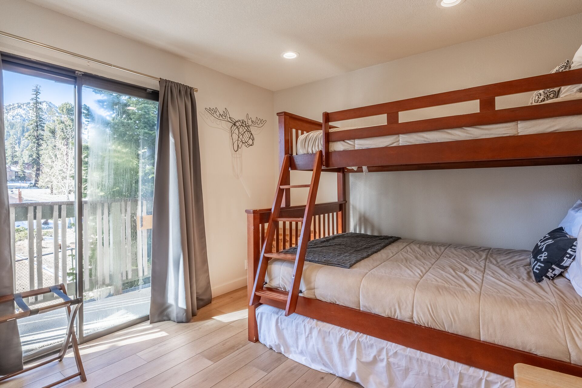 A bunk bed with a ladder, a window with curtains, and a view of a residential area.
