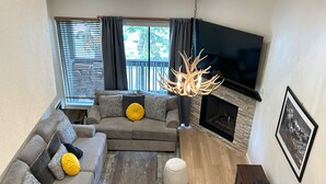 A living room with a sectional sofa, a fireplace, a mounted TV, and a wooden coffee table. - Bacta Haus 3br/3ba+Loft walk to Village & Canyon (Mammoth Lakes)