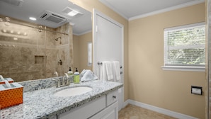 A bathroom with a marble countertop, a sink, a shower with a glass door, and a window with blinds.