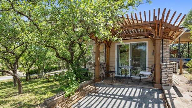 A covered patio area with a pergola, outdoor seating, and a stone building with glass doors.