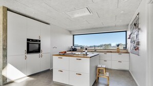 Una cocina moderna con armarios blancos, horno integrado, un ventanal con vistas y un taburete de madera.