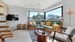 Una sala de estar moderna con un ventanal grande, un sofá, una mesa de centro y un televisor montado en la pared.