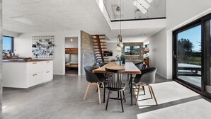 Una cocina moderna con una isla central, una zona de comedor con mesa y sillas de madera, y un amplio ventanal corredero que da a un balcón.