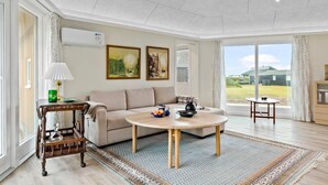 Ein geräumiges Wohnzimmer mit einem beigefarbenen Sofa, einem runden Couchtisch und Blick ins Freie durch große Fenster.