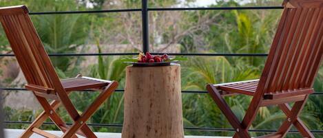 Two wooden chairs with a small table between them, placed on a balcony with a view of lush greenery.